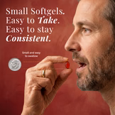 Man holding a small softgel pill next to a coin for size comparison on a red background.
